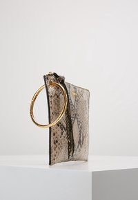Pochette con texture in pelle di serpente beige e nera, con manico ad anello in metallo dorato e chiusura con zip. Presenta una leggera goffratura sulla superficie.