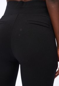 Czarne legginsy o wysokim stanowiące z gładkiej tkaniny, z dwoma tylnymi kieszeniami i bezszwowym wykończeniem sięgającym do kostek.