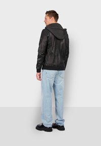 Sort læderjakke med en grå hættetrøje, der har en tætsiddende pasform, ribbede manchetter og en glat overflade. Båret sammen med lyseblå jeans og sorte støvler.