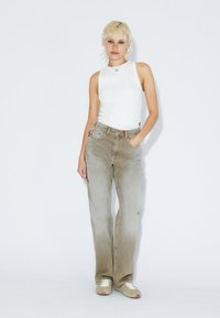 Jeans de cintura alta en gris claro, con un diseño de pierna recta, un ligero desvanecimiento y un estilo clásico de cinco bolsillos. Combinados con una blusa sin mangas blanca.