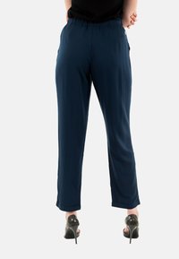 Pantalones ligeros de color azul marino con cintura elástica, diseño de pierna recta y bolsillos laterales, combinados con zapatos de tacón altos negros.