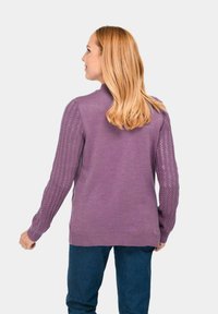 Paarse trui met een geweven, open breiwerkontwerp op de mouwen, ribgebreide manchetten en onderrand. Gestyled met donkerblauwe jeans. Van achter bekeken.