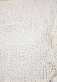 Il maglione bianco all'uncinetto presenta un motivo geometrico con punti aperti, evidenziando un design texturizzato e un materiale in filato spesso e morbido.