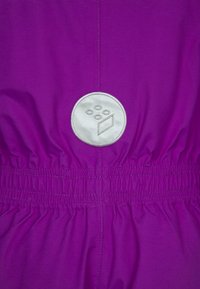 Żywo fioletowa kurtka z marszczonym pasem oraz okrągłą srebrną łatą z pięcioma małymi okręgami i prostokątnym wzorem. Gładka tekstura.