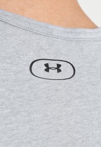 Grauer T-Shirt-Stoff mit glatter Textur, versehen mit einem schwarzen Under Armour-Logo in einer ovalen Umrandung nahe dem Kragen auf der Rückseite.