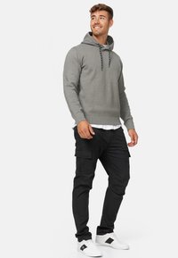 Grijze hoodie met een kangoeroe-pocket, capuchon met trekkoord en geribbelde zoom, gecombineerd met zwarte cargo broek met zijzakken en een taps toelopende pasvorm.