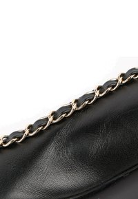 Chaussure en cuir noir avec une chaîne dorée décorative tissée avec des bandes de cuir noir le long du bord.