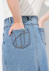 Vaaleansininen farkuhame, jossa on korkea vyötärö. Takana on kaksi taskua ruskealla ompelella ja suora leikkaus. Suora ja sileä pinta.