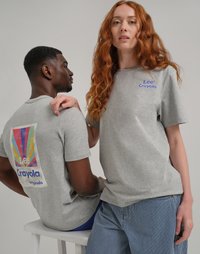 T-shirt grigi in cotone presentano una grafica colorata di Crayola sul retro e un logo blu sul fronte. Il modello indossa pantaloni a righe.