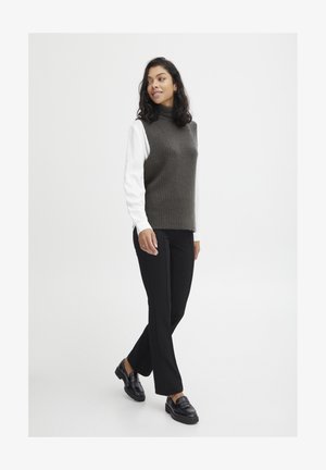 Dunkelgrüner gerippter ärmelloser Rollkragenpullover kombiniert mit einem weißen Langarmshirt und schwarzen maßgeschneiderten Hosen. Schwarze Loafers runden den Look ab.