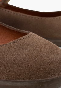 Braune Wildleder-Ballerinas mit spitzem Fuß, die eine glatte Textur und dezente Nähte entlang der Kante aufweisen. Einfaches, minimalistisches Design.