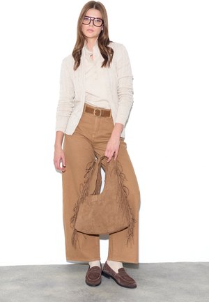 Woman wearing beige cardigan, tan wide-leg pants, and brown loafers, holding a large brown fringed suede handbag.