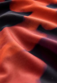 Close-up of red and black soft fabric with a mesh texture and subtle folds creating light and shadow patterns.