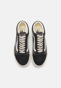 Baskets en daim noir avec une bande blanche, dotées de lacets beiges et d'une tige texturée. Intérieur crème remarquable et détails de couture.