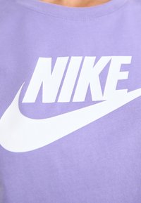 Purpurna bombažna majica z velikim belim logotipom "NIKE" v drznem fontu in obliko zamaška, ki prikazuje sproščen športni slog.