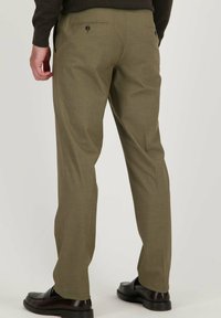 Pantalon vert olive en tissu texturé, doté de deux poches arrière avec boutons et d'un design à jambes droites. Accompagné de chaussures foncées.