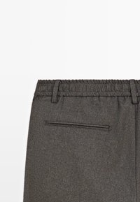 Pantaloni grigi con vita elastica, tessuto testurizzato, parte frontale piatta e una singola tasca con zip discreta sul retro.