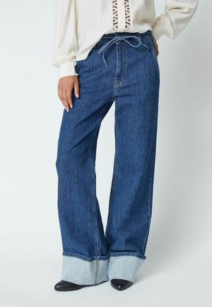 Wide-legged denim jeans with a high waist, blue fabric, and contrasting light blue cuff. Ties at the waist and stitched details visible.