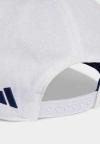 White cap with textured fabric, featuring a navy logo and adjustable white plastic strap at the back with multiple snaps.