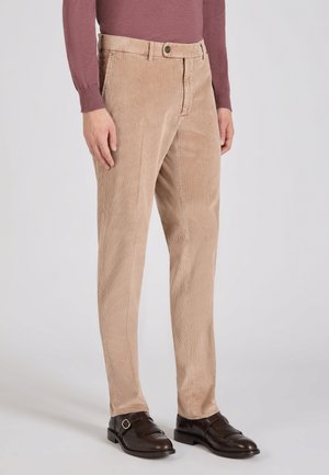 Beige corduroy broek met smalle verticale strepen, vlakke voorkant en een enkele knoopsluiting. Gecombineerd met donkerbruin geklede schoenen.