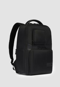 Mochila negra con tela texturizada, múltiples compartimentos con cremallera, correas acolchadas y asa superior. Diseño rectangular elegante con acentos mínimos.