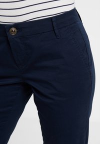 Náměsíčné modré kalhoty s hladkou bavlněnou texturou, vybavené přední knoflíkovou a zipovou zapínací soupravou, bočními kapsami a designem slim-fit.