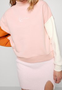 Felpa in misto cotone con collo alto, caratterizzata da un corpo rosa, maniche arancioni e bianche, e un logo bianco al centro.