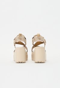 Beige Plattformsandalen mit einem strukturierten Stoffobermaterial, verstellbaren Riemen und einer klobigen, strukturierten Sohle. Dekorative Akzente an den Riemen.
