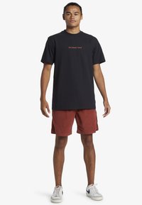 Black cotton t-shirt with orange "Quiksilver" logo, paired with rust-colored corduroy shorts and white sneakers. Simple, relaxed fit.
