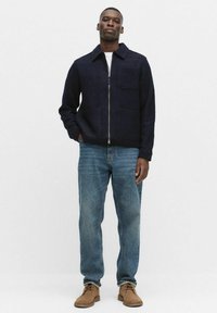 Laikku sininen villasekoite takki, jossa on vetskari, kaulus ja kaksi etutaskua, yhdistettynä vaaleansinisiin farkkuihin ja ruskeisiin nahkakenkiin.