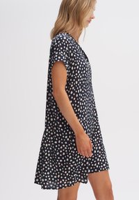 Marineblaues Kleid mit weißen und rosa Punkten, kurzen Ärmeln, lockerer Passform und knielangem Design. Hergestellt aus leichtem, seidigem Material.