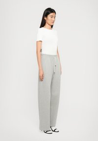 Hvid kortærmet top parret med grå brede sweatpants. Bukserne har en elastisk talje med snøre. Modellen står sidelæns.