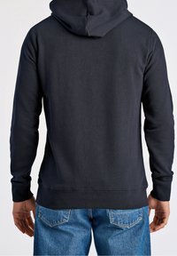 Tmavá mikina s kapucí a hladkou texturou, s dlouhými rukávy a středně dlouhým lemem. Doplněno modrými džínami.
