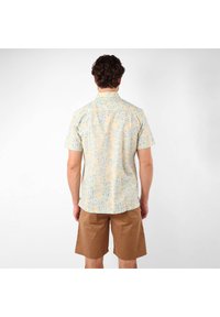 Chemise à manches courtes de couleur jaune clair avec un motif floral bleu, en matériau coton, coupe décontractée, col à boutons, associée à un short marron.