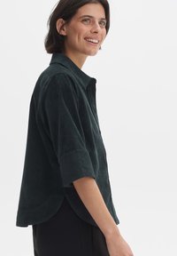 Dark green corduroy shirt with a collar, button front, and rolled sleeves; features a slightly curved hem and soft texture.