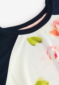 Laine ja valge lühikeste varrukatega topp, millel on roosa ja rohelise lillemustriga dekoratsioon, ümmargune kaelus ja pehme kangateks.