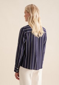 Camicia a maniche lunghe blu navy con motivo a catena verticale bianco, polsini con bottoni e taglio dritto, realizzata in tessuto leggero e liscio.