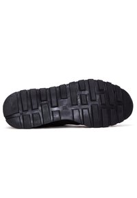 Semelle de chaussure de sport noire en caoutchouc texturé, avec des crampons définis et une forme solide et plate pour une meilleure traction et stabilité.