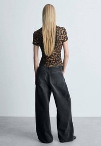 Top ajustado de manga corta con estampado de leopardo y escote redondo, combinado con unos vaqueros de mezclilla negros de tiro alto y corte holgado.