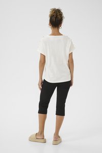 White short-sleeve top with a round neckline; features decorative buttons on shoulders. Worn with black capri pants and straw-platform sandals.