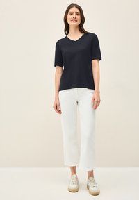 T-shirt a V blu navy con maniche corte, abbinato a pantaloni bianchi a tre quarti e sneakers beige. Il tessuto sembra leggero e morbido.