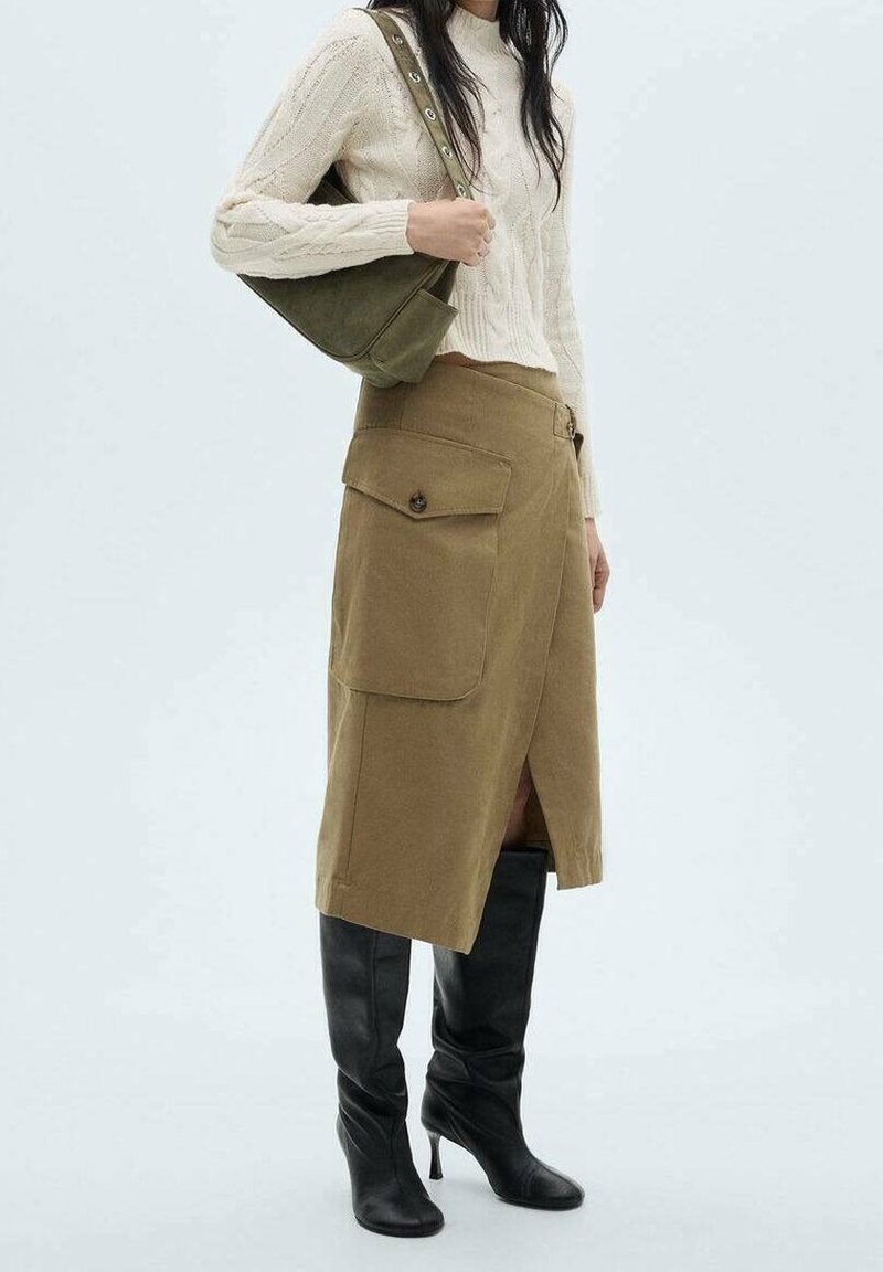 Falda midi caqui con bolsillos laterales, combinada con un suéter de punto trenzado color crema y botas altas negras. Un bolso verde olivo completa el look.