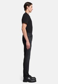 Zwarte t-shirt en donkergrijze jeans met een slim fit, zijaanzicht weergegeven. Zwarte schoenen met een dikke zool maken de look af.