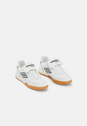 White athletic shoes with a rubber gum sole, featuring a black and white logo, lace-up front, and velcro strap for added support.