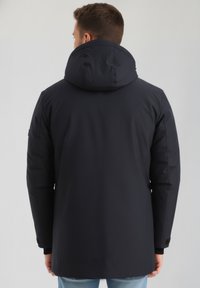 Jūras spēku zilas krāsas kapucīna jaka ar gludu tekstūru, kas piedāvā taisnu griezumu un elastīgas aproces. Izstrādāta siltumam un komfortam.