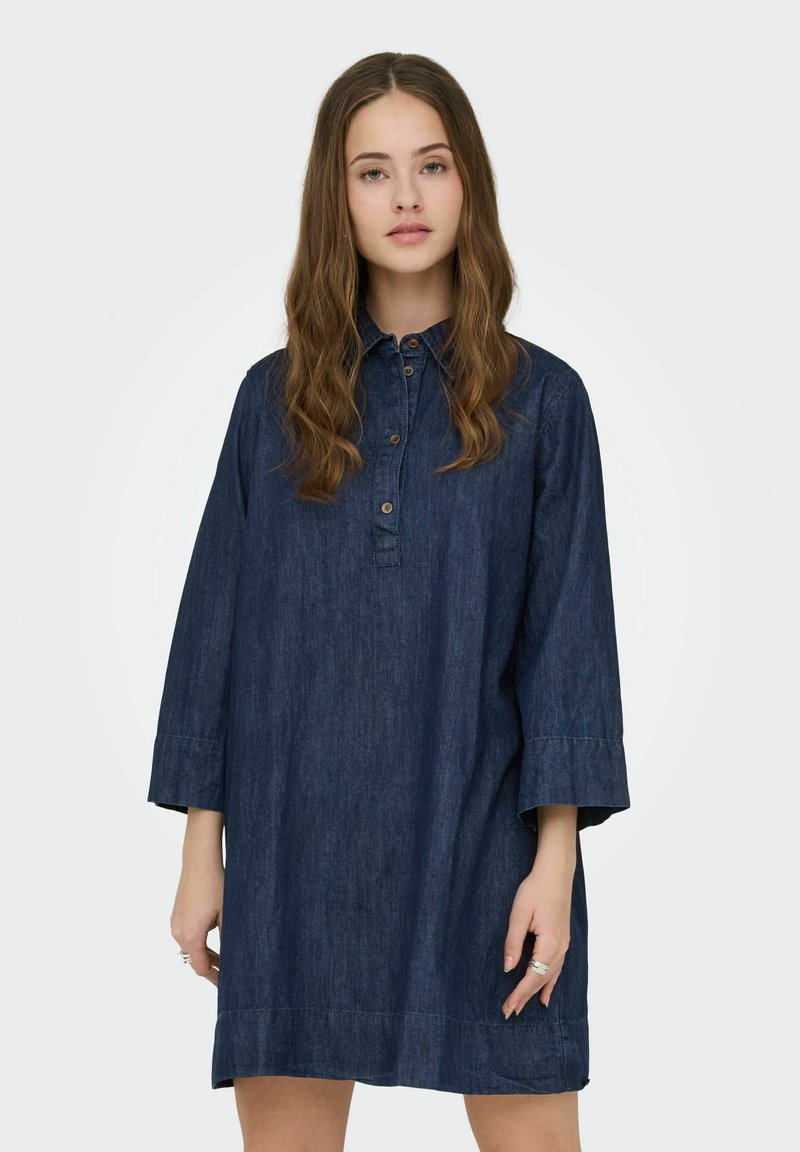 Robe chemise en denim avec col à boutons, manches trois-quarts et coupe ample. Couleur bleu profond avec une texture lisse et un design minimaliste.