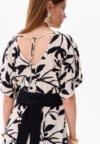Zwart-wit bloemenpatroon jurk met een diepe V-rug, korte puffmouwen, en een zwarte tailleband die aan de achterkant in een strik is geknoopt.