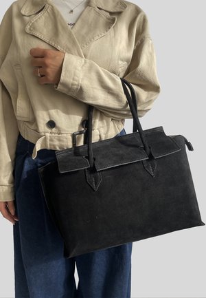 Borsa in suede nera con due manici, una patta superiore e dettagli a punta. Presenta una texture liscia e una forma rettangolare ben strutturata.
