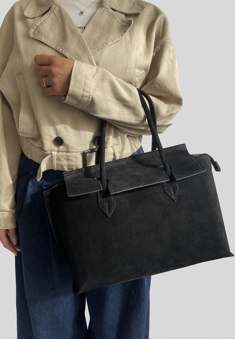 Borsa in suede nera con due manici, una patta superiore e dettagli a punta. Presenta una texture liscia e una forma rettangolare ben strutturata.