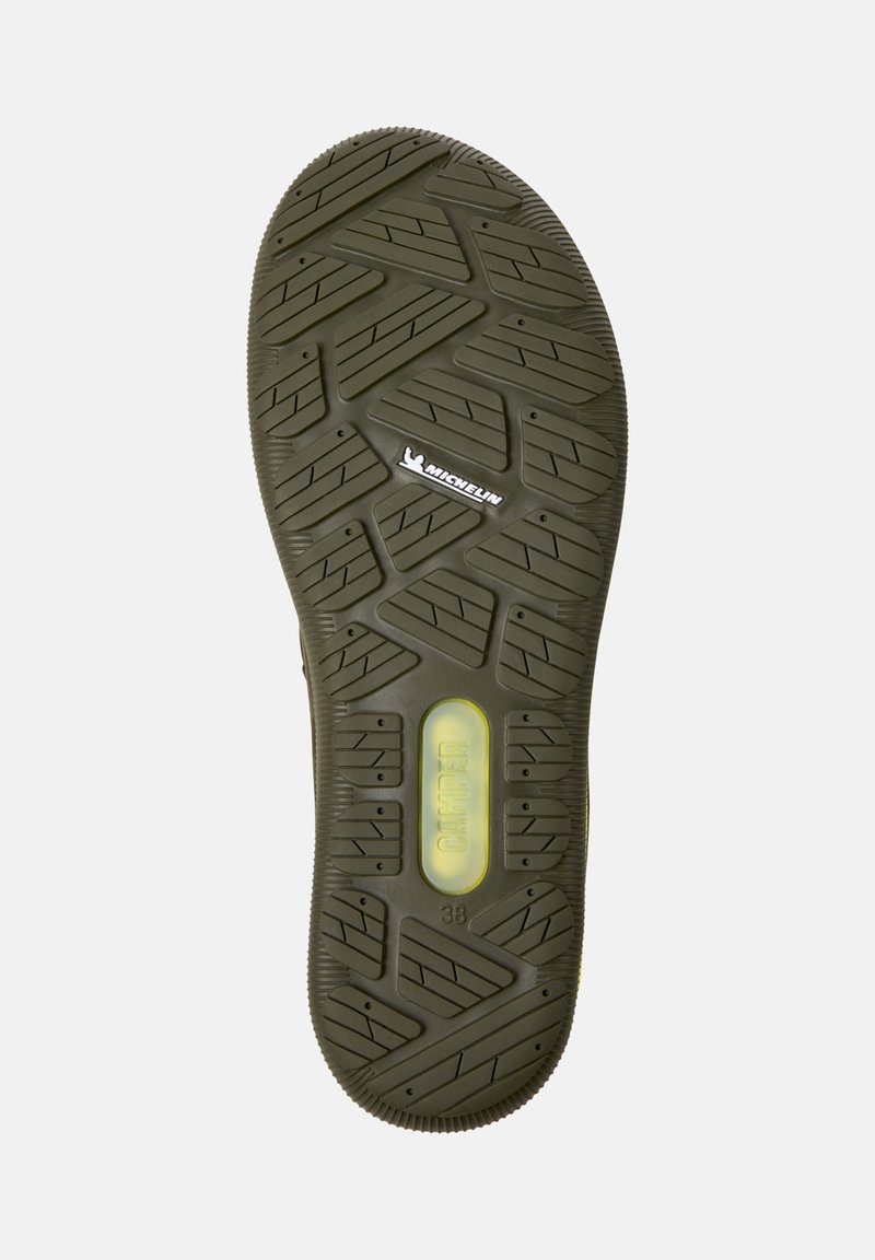 De zool van een schoen heeft een gestructureerd ontwerp met diepe groeven, het Michelin-logo en gele demping gemarkeerd met "CAMPER" maat 38.